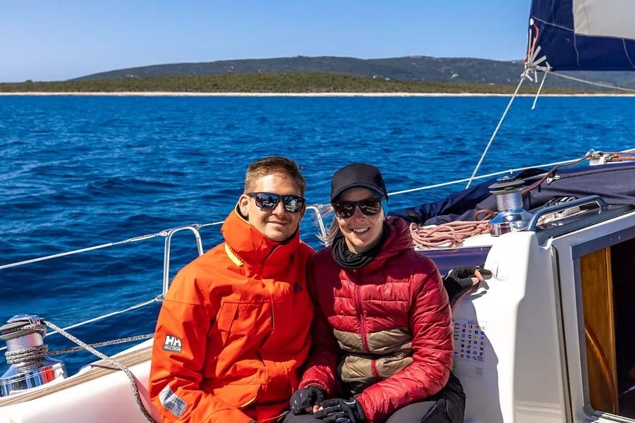 Zwei Crewmitglieder beim Segeln, Küste im Hintergrund